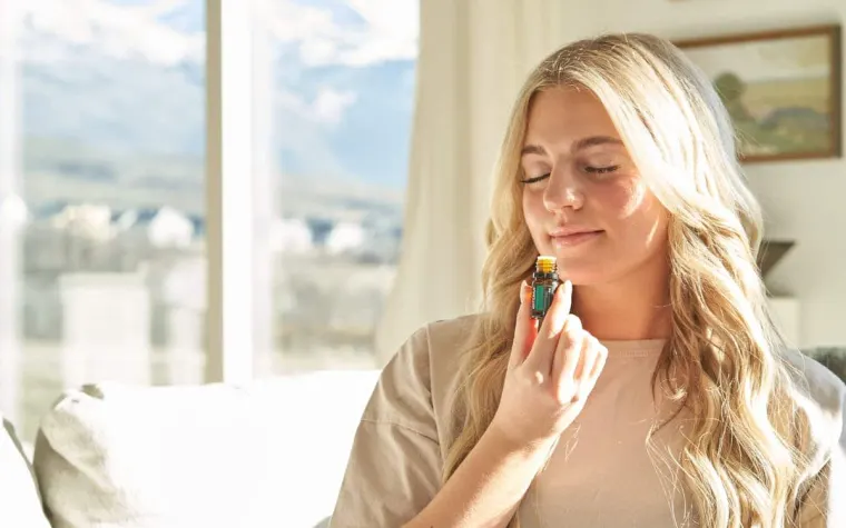 Una mujer huele un frasco de perfume junto a una ventana